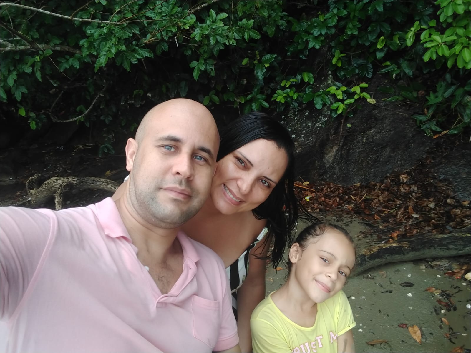 Marcia está no centro da imagem, com uma blusa de alça listrada preta e branca. Ao seu lado direito está a filha Lara, uma criança que usa camiseta amarela. Ao lado esquerdo de Marcia está o marido Jimmy, um homem alto, careca e de olhos azuis. Ao fundo há uma vegetação